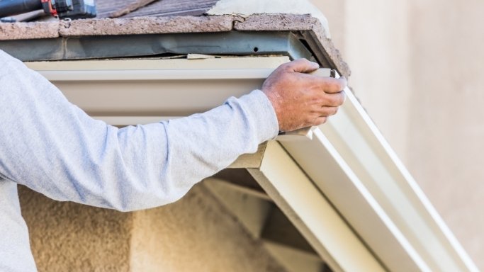 New black guttering being fitted along a freshly painted fascia board